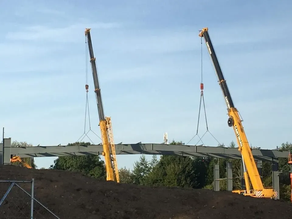 Deux grues en tandem soulèvent une charpente métallique