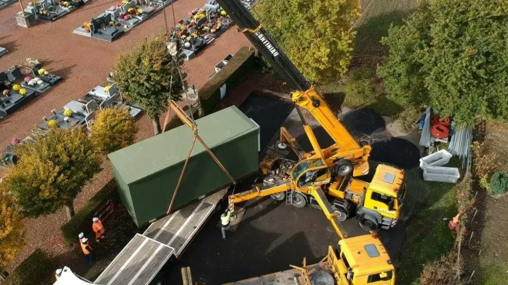 Vue aérienne d’un module suspendu à une grue Cantiniau près d’une remorque et d’un mur
